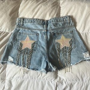 Blue jean shorts, with stars on back pockets. Silver fringes hanging off pocket.
